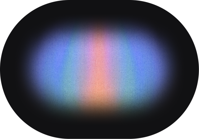An abstract gradient design featuring a rounded rectangular or pill-shaped form on a black background. The gradient creates a soft, glowing effect that emanates from the center outward, transitioning through multiple colors. The central area glows with a warm peach or coral tone, which gradually blends into blue hues on the left and right sides. Touches of green and turquoise appear in the transition zones between the blue and coral areas. The edges of the rounded rectangle fade smoothly into the black background, creating a diffused, ethereal appearance reminiscent of an aurora or color spectrum. The overall effect is smooth and luminous, with no visible text or UI elements.